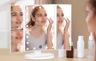 a person looking into a trifold mirror on a vanity