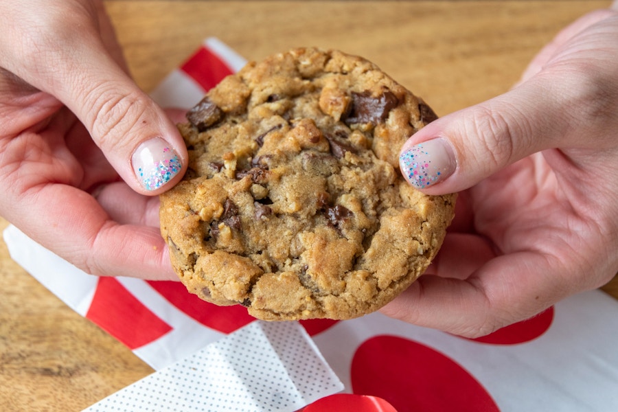 A person's hands holding a Chick-fil-A chocolate chunk cookie over a table.