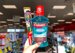 hand holding a Colgate manual toothbrush and Colgate mouthwash