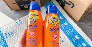 Someone holding two bottles of Banana Boat sunscreen above some Amazon packaging