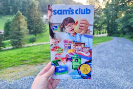 person holding the sams club instant savings book in front of trees