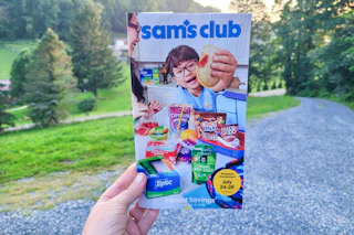 person holding the sams club instant savings book in front of trees