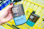 hand holding up an every man jack body wash above a yellow shopping cart
