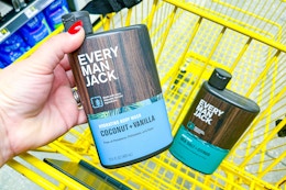 hand holding up an every man jack body wash above a yellow shopping cart