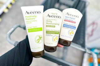 person holding aveeno skincare products over a cart