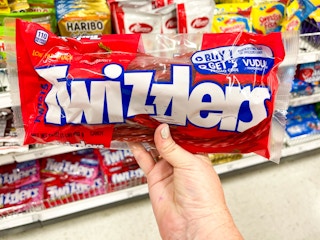 a person holding twizzlers in store by cart