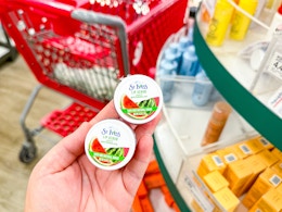 hand holding 2 st ives lip scrubs in front of a target cart