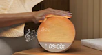 a hand tapping an sunrise alarm clock on a nightstand 