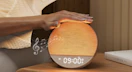 a hand tapping an sunrise alarm clock on a nightstand