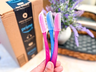 a hand holding three dermaplanning razors in front of an Amazon box