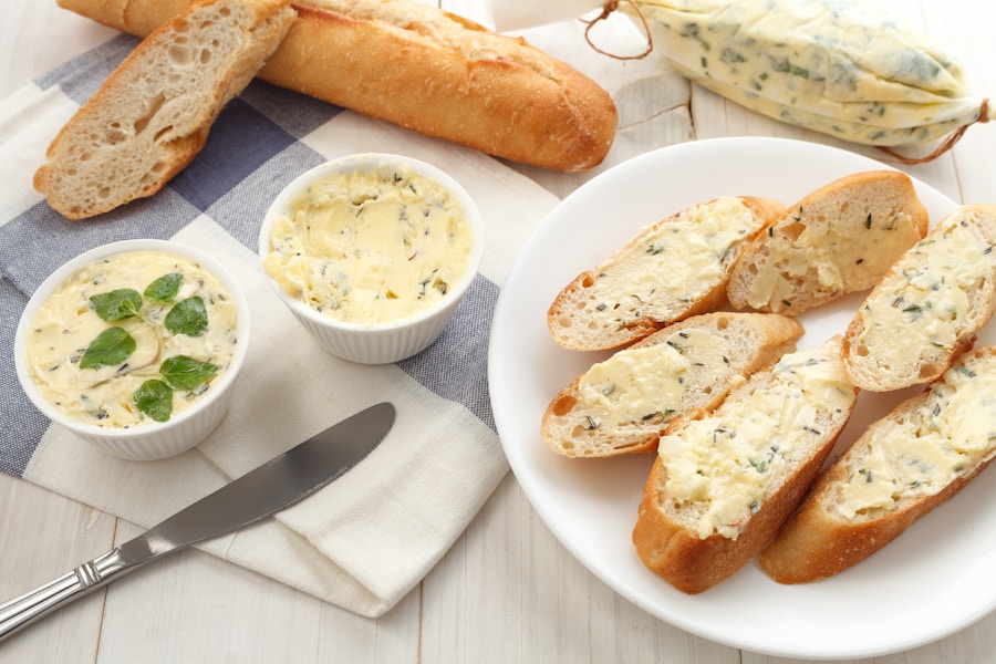 Dishes of compound butter on a table next to slices of bread that have been buttered.