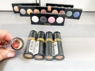 hand holding revlon lipstick with eyeshadow quads in background on walmart shelf