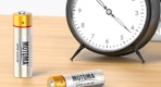 batteries next to a clock on a wooden desk
