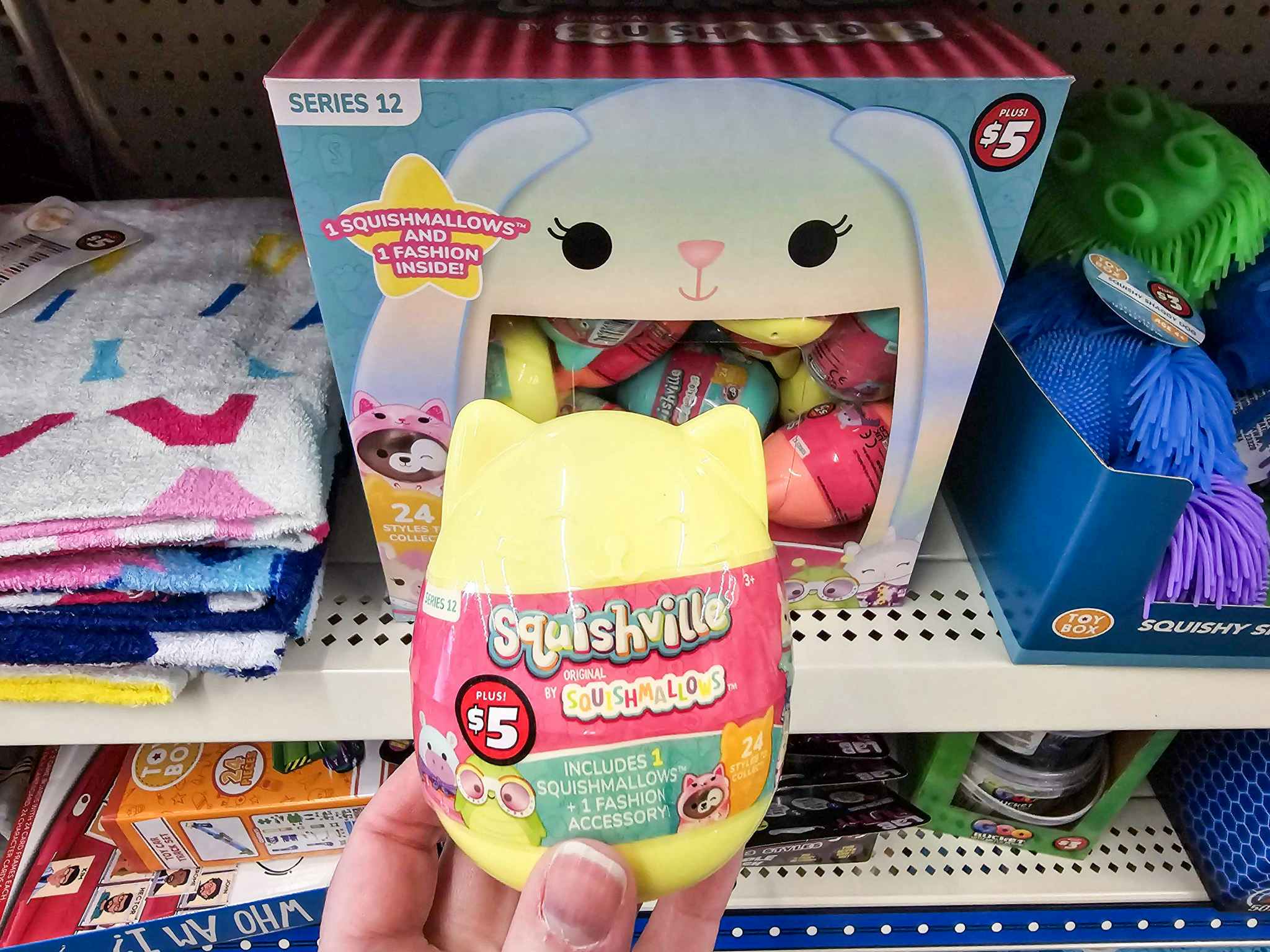 person holding a squishville by squishmallows toy in front of the display box on a shelf
