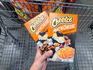 hand holding two boxes of mac n cheese in front of cart