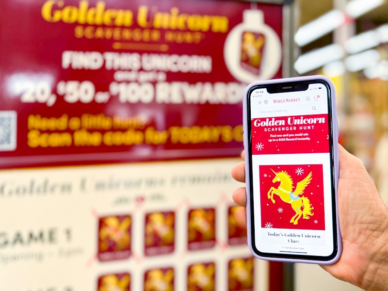 hand holding a phone next to world market golden unicorn scavenger hunt signage