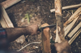 A man using a Gerber tactical knife on wood outside.