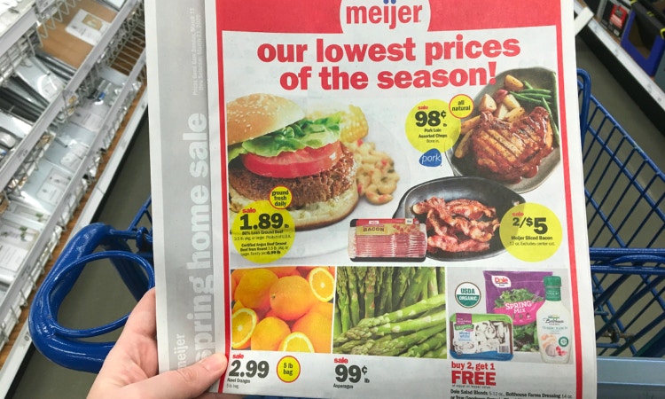 Hand holding a Meijer circular in front of a Meijer cart in store