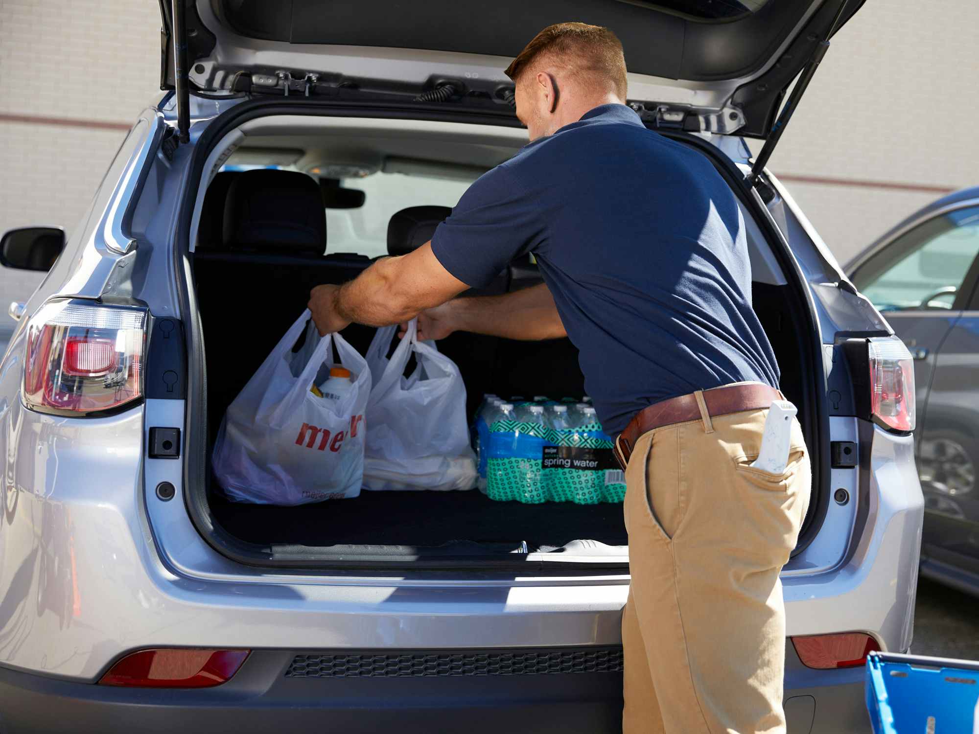 someone putting bags of items from Meijer into a trunk