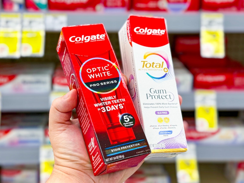 person holding 2 colgate premium toothpastes in front of a shelf