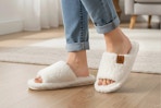 Lifestyle image of a woman wearing a pair of the white Ecetana House Slippers in home setting (close up shot)
