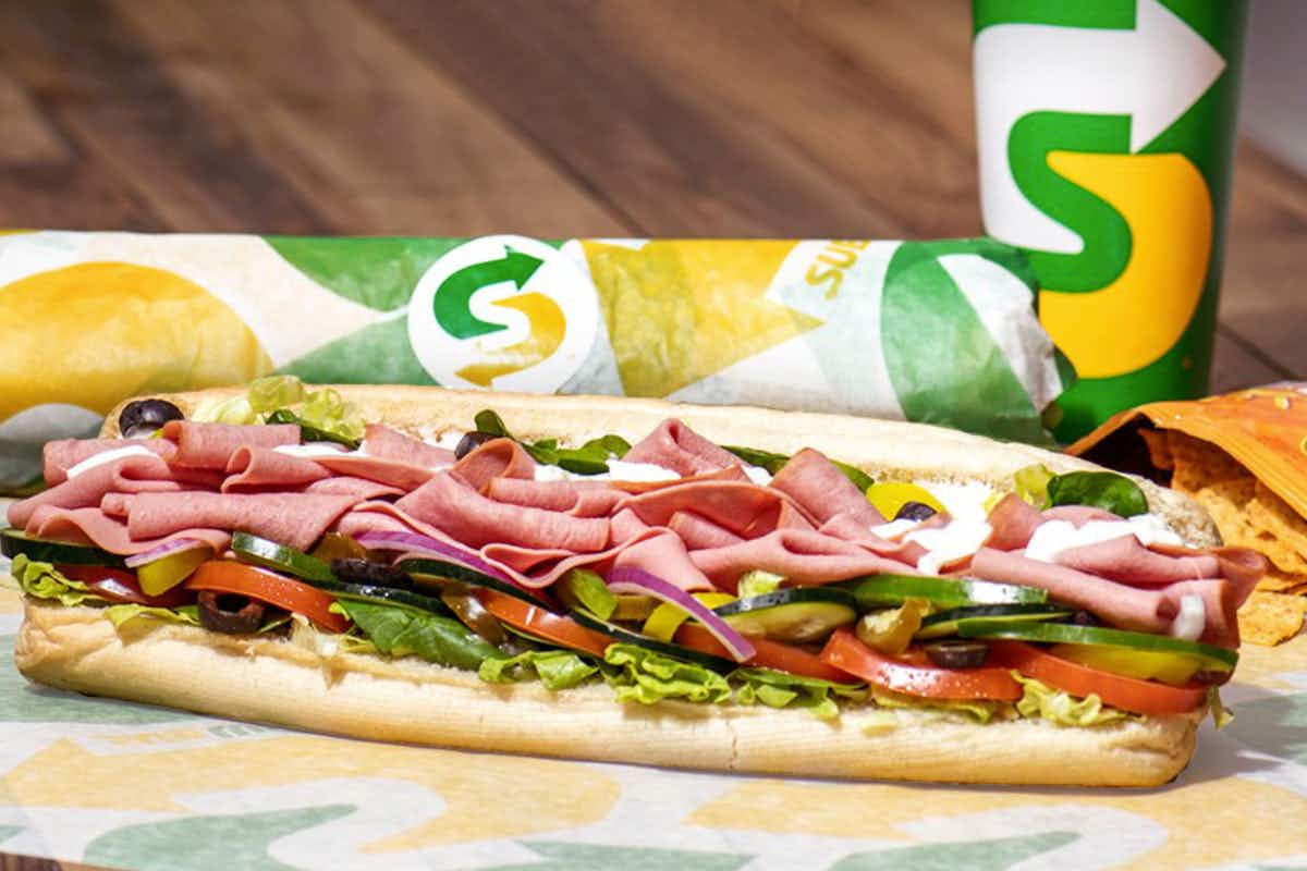 two subways sandwiches and a drink on table 