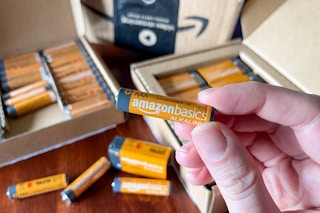 A person holding up an orange amazon basics battery with an open box of batteries in the background.