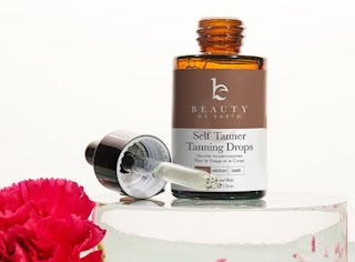 a brown bottle next to a dropper on display with a pink flower