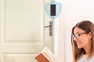 A woman reads a book by a door that is protected by a reinforcement lock.