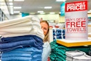 A person holding up a stack of towels next to a buy 1 get 2 free towels sale sign inside JcPenney. 