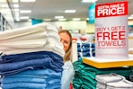 A person holding up a stack of towels next to a buy 1 get 2 free towels sale sign inside JcPenney.