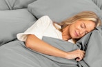 a person laying in a bed with grey sheets