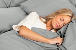 a person laying in a bed with grey sheets