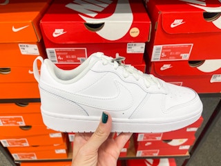 A Nike Airforce One shoe held out in front of multiple Nike boxes.