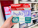 hand holding colgate, tom's of maine, and hello toothpaste at target