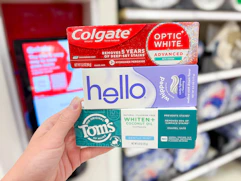 hand holding colgate, tom's of maine, and hello toothpaste at target