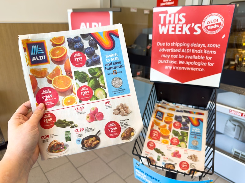 Someone taking a This Weeks ALDI ad from the basket in the entrance of ALDI