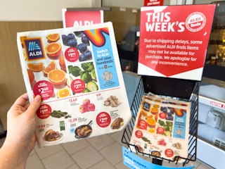 Someone taking a This Weeks ALDI ad from the basket in the entrance of ALDI