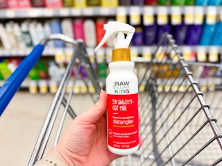 person holding a bottle of raw sugar hair detangler over a cart