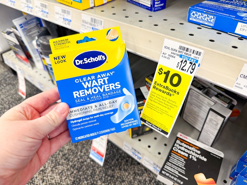 person holding a box of dr scholls wart remover by a sign for $10 extrabucks