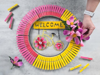 person making bright spring wreath with dollar tree garden sign and painted clothespins