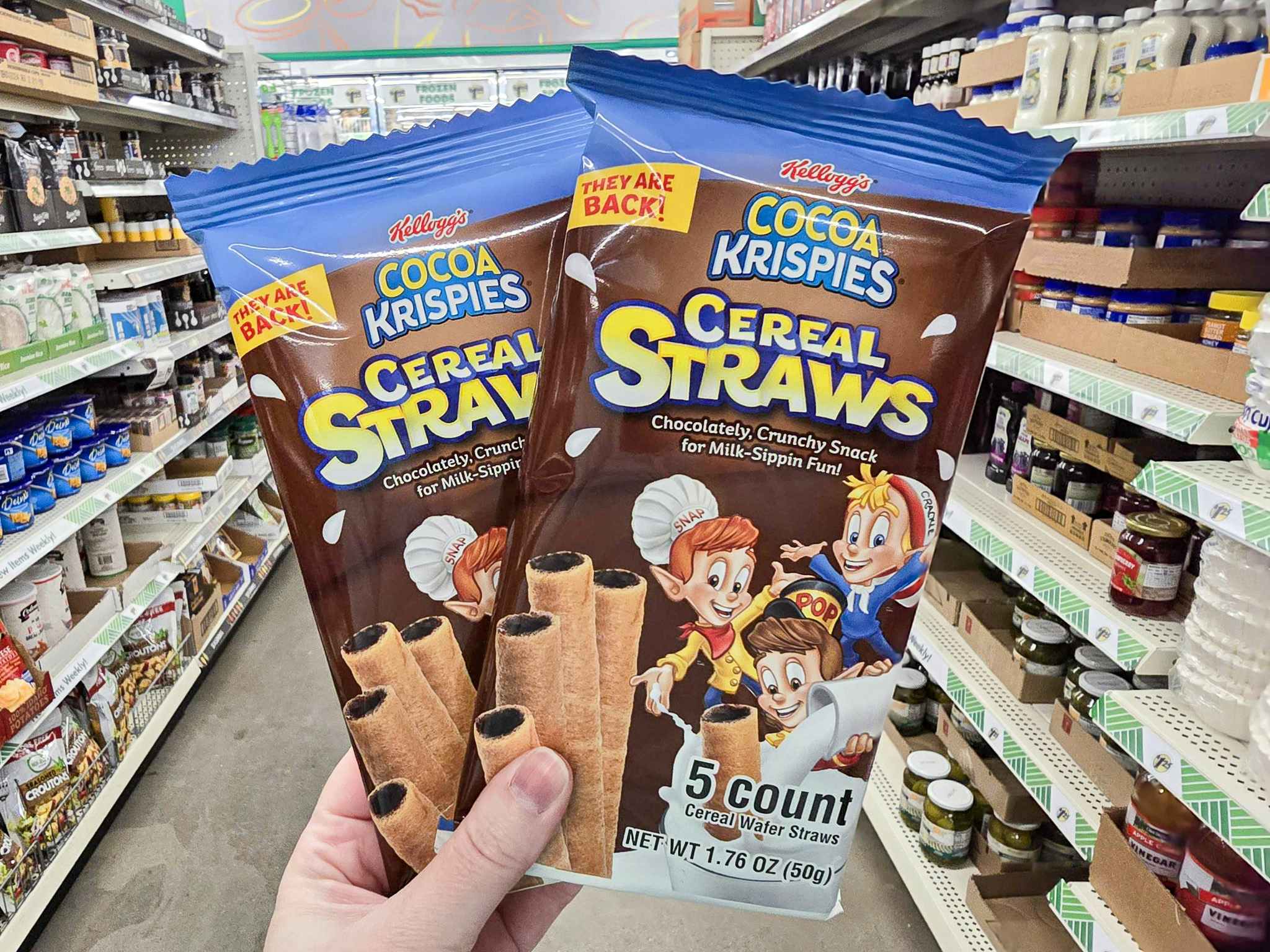 person holding 2 packs of cocoa krispies cereal straws in an aisle