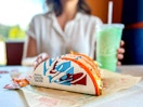 a person sitting at taco bell with doritos locos tacos and a baja freeze
