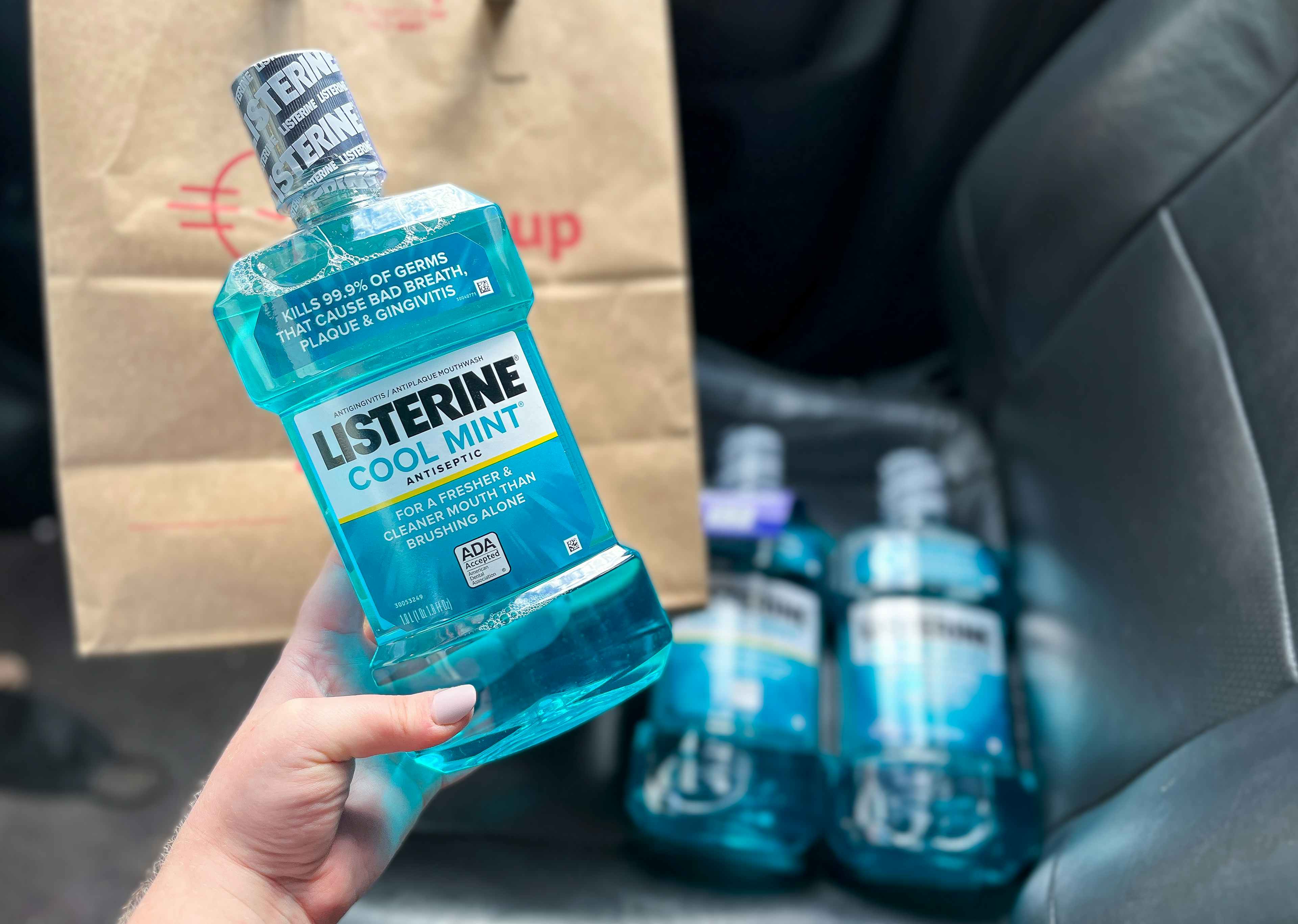 hand holding a bottle of listerine mouthwash in front of a walgreens pickup bag in a car