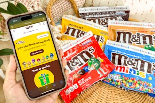 someone holding a phone showing the M&Ms rewards club site next to a variety of M&M candy