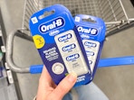 hand holding two packs of oral b glide dental floss on walmart cart