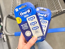hand holding two packs of oral b glide dental floss on walmart cart