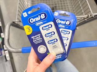 hand holding two packs of oral b glide dental floss on walmart cart