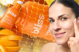 A bottle of Bliss brightening serum sits on top of a sliced orange as a woman rubs cream on her cheek. Oranges, more Bliss in background.