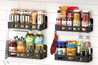 Four dark grey racks filled with spices and kitchen essentials hang on a white brick wall